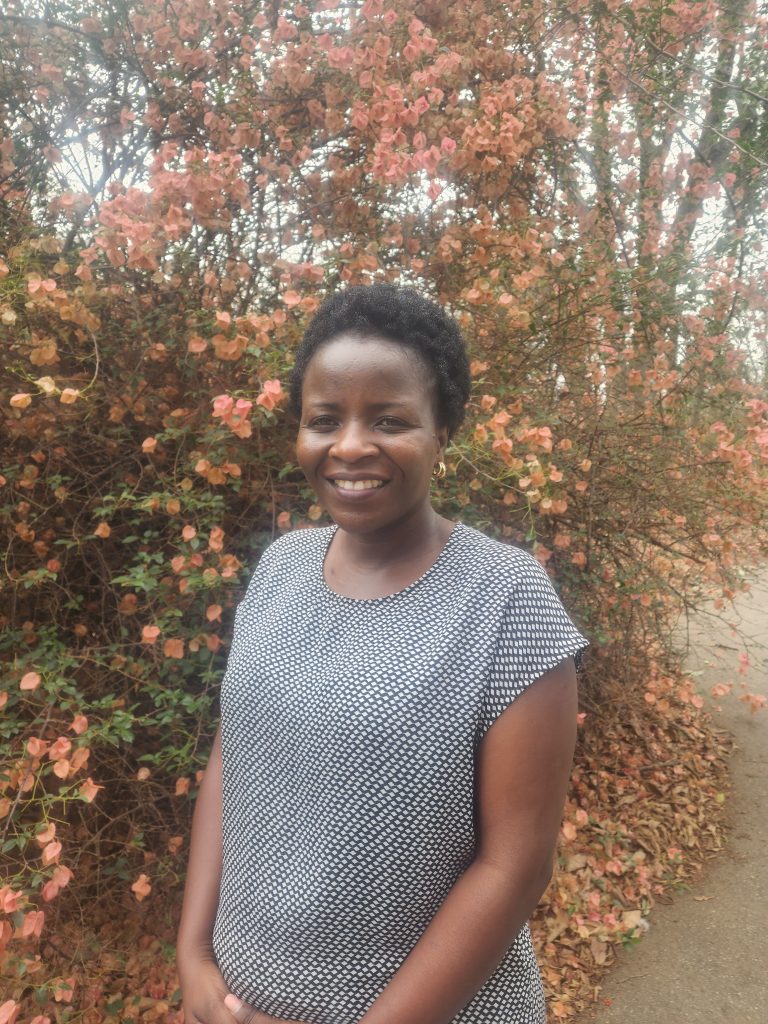 Lovelater Sebele stands smiling against a background of trees.